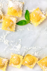 Ravioli with flour and basil leaves, forming a frame, shot from the top on a white marble table with a place for text, a design template for a recipe