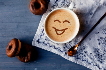 Happy cup filled with coffee on blue wooden table with donuts
