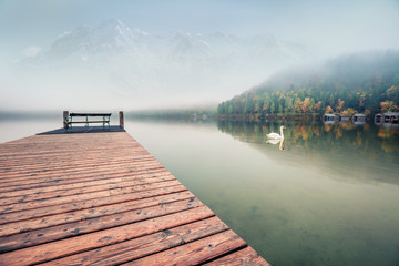 Fantastic autumn scene of Altausseer See lake with Trisselwand peak in the fog on background. Misty morning view of Altaussee village, district of Liezen in Styria, Austria, Europe.