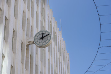 A public clock on the side of a white city building against a blue cloudless sky