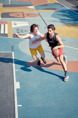 Top view of two men playing basketball on playground in morning .