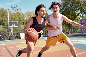 Picture of young sports men playing basketball on playground on summer day.
