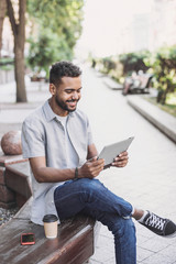 Young handsome men using digital tablet in a city. Smiling student man having coffee break. Modern...