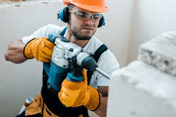 selective focus of handsome handyman in uniform and yellow gloves using hammer drill