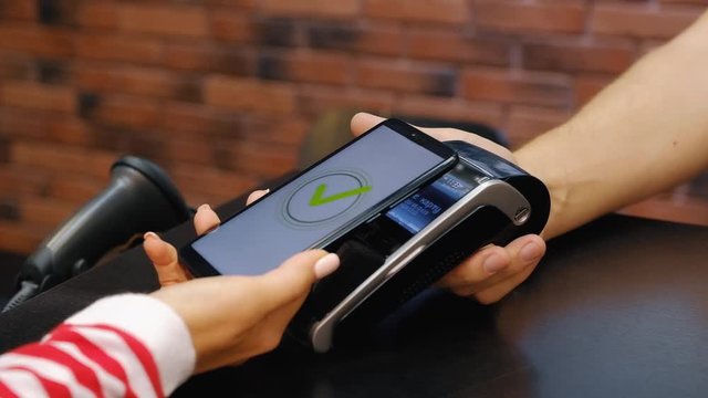 Hand of young woman pays for purchases using the contactless payment nfs system