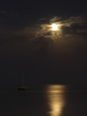 Lonely yacht with lowered sails is illuminated by the moon against a cloudy sky and the night sea © TETIANA