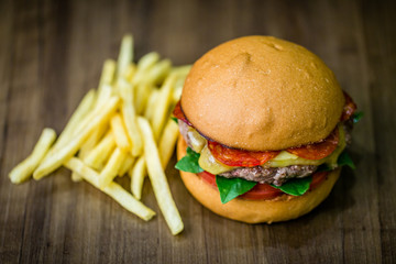 Craft beef burger with cheese, italian peperoni, tomato, basil leafs and french fries on wood table and rustic background.