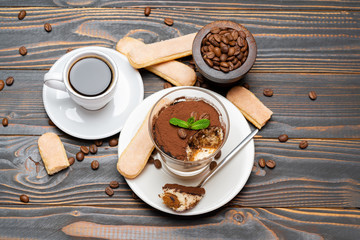 Portion of Classic tiramisu dessert in a glass, cup of coffee and savoiardi cookies on wooden background