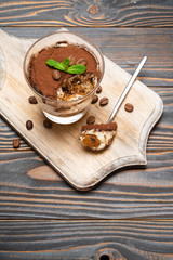 Portion of Classic tiramisu dessert in a glass cup on cutting board on wooden background