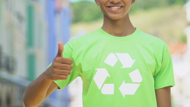 Boy in green shirt with recycle symbol showing thumbs up, environment protection
