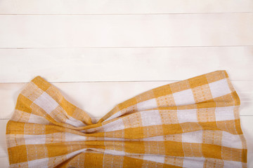 A cotton tablecloth with yellow cells lies on a white wooden background. Horizontally. View from above.