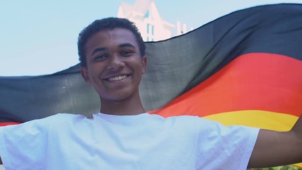 Afro-American teenager boy waving German flag outdoors, national holiday - Powered by Adobe