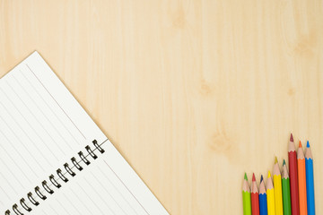 colorful pencils and notebook on wooden background top view. art equipment.