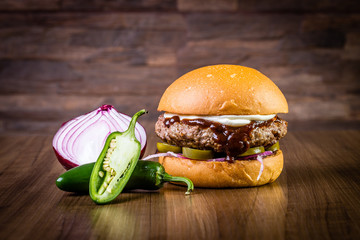 Craft beef burger with cream cheese, purple onion, jalapeno pepper on wood table and rustic background. - obrazy, fototapety, plakaty