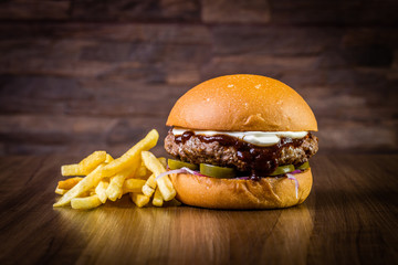 Craft beef burger with cream cheese, purple onion, jalapeno pepper and french fries  on wood table...