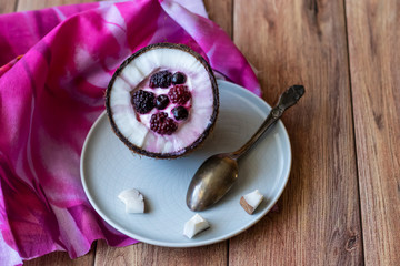 Berry dessert with yogurt in a cup of coconut on a wooden background. Blackberries, raspberries, blueberries, black currants.