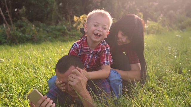 happy family teamwork outdoors have fun concept outdoors slow motion video. mom dad and son take a photo with a smartphone in nature are sitting on the grass have fun lifestyle playing .mom girl dad