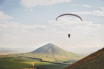A white-orange paraglider flies over the mountainous terrain