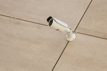 Bottom view of beige tiled wall with white safety camera on it