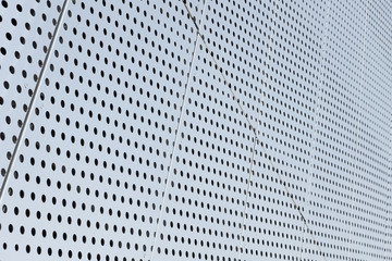 Diagonal view of metall grilles and round holes in metal surface, perforated panels for background.