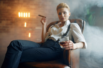 Woman sitting in chair with whiskey and cigar - obrazy, fototapety, plakaty