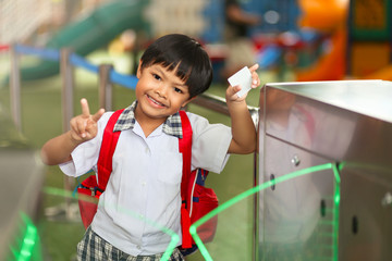 An Asian young schoolboy holding a keycard at pedestrian access control flap barriers in a school. 