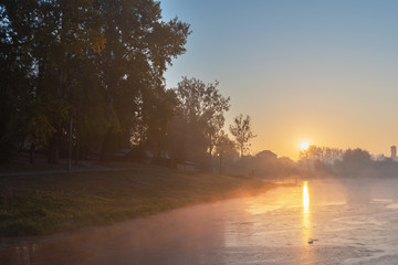 Magical autumn morning on a lake covered with fog with golden trees around