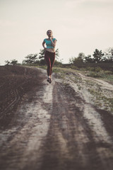 young woman in sportswear running distance in the field, girl engaged in sport outdoors on a cloudy day, concept healthy lifestyle and bodycare