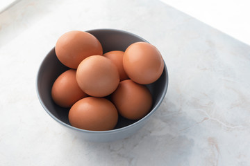 Organic eggs in gray bowl on white marble table background. Farm products, domestic life
