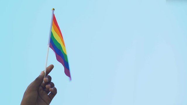 Hand of African-American male holding rainbow flag against sky, lgbt rights