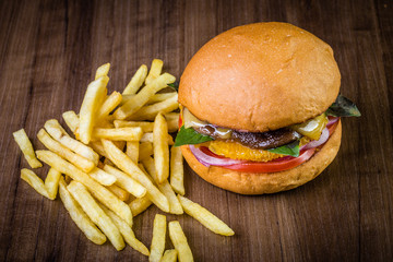 Vegetarian craft burger with cheese, orange, basil leafs, shiitake mushroom, purple onion and french fries on wood table and rustic background.