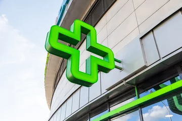 Fotobehang Apotheek Close-up van groen kruis - teken van apotheek op glazen gebouw