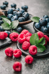 Fresh berries with raspberries, blueberries, blackberries in bowl on a stone stand on a dark metal background.