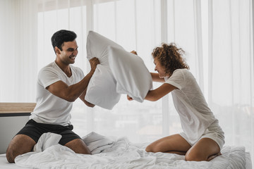 a man and a woman playing pillow on the bed