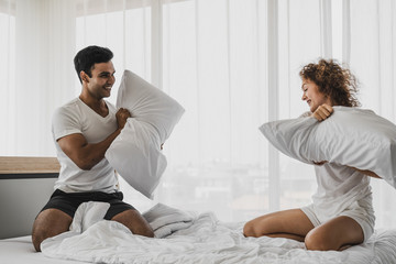 a man and a woman playing pillow on the bed