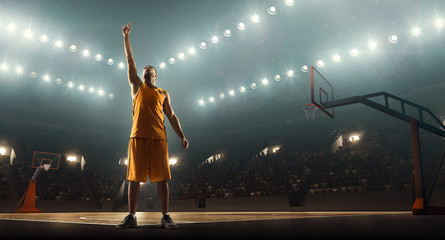 Fototapeta na wymiar Basketball player on a crowded and floodlit basketball court celebrates championship