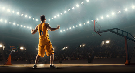 Fototapeta na wymiar Basketball player on a crowded and floodlit basketball arena celebrates victory