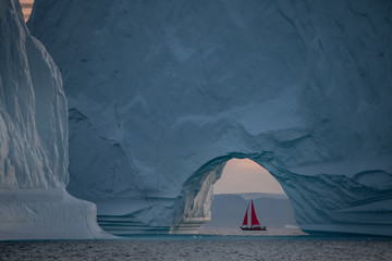Red sail and large iceberg landscape during mid night sun