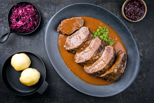 Traditioneller geschmorter marinierter deutscher Sauerbraten vom Rind mit Blaukraut und Kartoffel Kn&ouml;del in w&uuml;rziger brauner Sauce als Draufsicht in einem Modern Design Teller