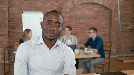 Confident Successful African Team Leader Portrait. Happy Young Man Smiles with his Diverse Team at Background in Loft Office. 4K Static Medium Shot