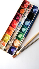 Paints for painting. Materials for drawing. Old watercolor paints and brushes on a white background.