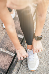 Close up shot of sportswoman's hands tying shoelaces. Female athlete getting ready for running in the city park and doing exercises. Running and sport concept. Vertical shot