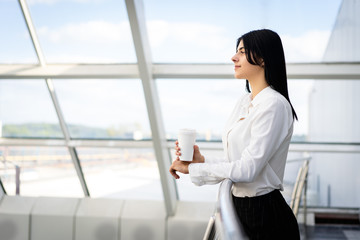 young woman with cup of coffee, looking forward, resting from the work, thinking of something inspirational. She are happy. Girl worker with cup of drink in hands