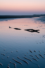 Receding blue waters through a log on a beach