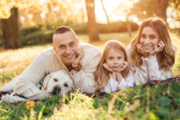 Happy family is having fun with dog labrador are lying on green grass in park.