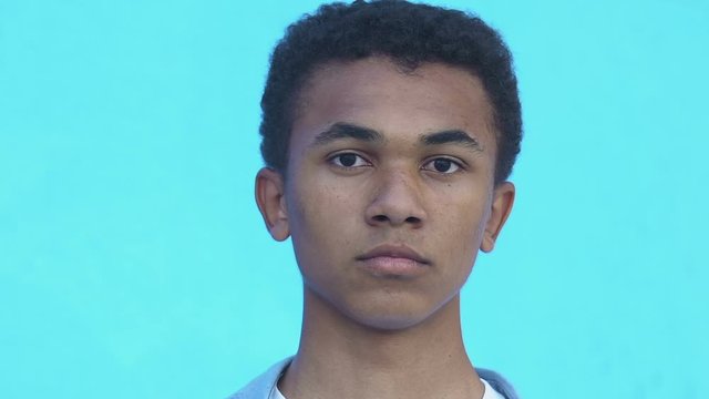 Upset African-American male teenager looking at camera against blue background