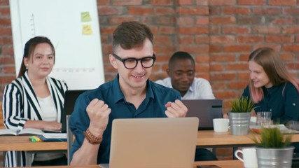 Excited Young Man with Laptop, Cheering and Celebrating Success or Business Win with Multiethnic Diverse Team in Loft Office. Colleagues and Coworkers Applaud and Congratulate. 4K Corporate Shot