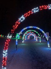 Colorful striped LED string light wrapped arches extend over a walkway at a holiday lights festival.