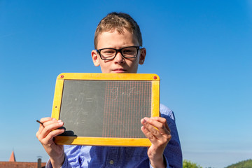 Boy with arithmetic problems on a blackboard with glasses in front of a blue sky