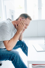 Fototapeta premium side view of handsome man in t-shirt with closed eyes touching head in apartment